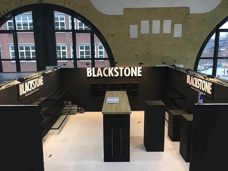 BLACKSTONE-stand met zwarte wanden, verlichte BLACKSTONE-belettering en een houten middentafel