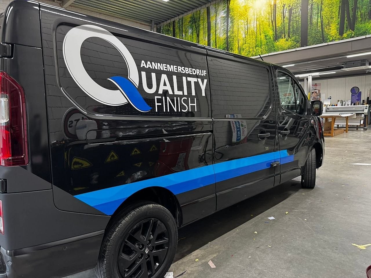 Zwarte Quality Finish-bedrijfsbus met het logo Aannemersbedrijf Quality Finish en een blauwe streep