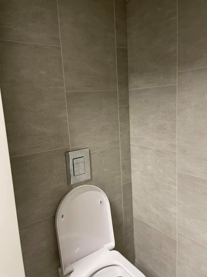 Toiletruimte met grote grijze wandtegels en een hangend toilet