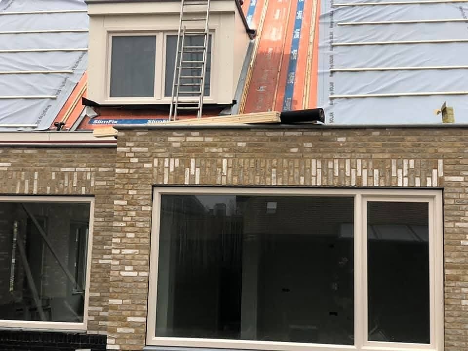 Dakkapel met ladder op een dak met dakfolie boven een gevel met grote kozijnen