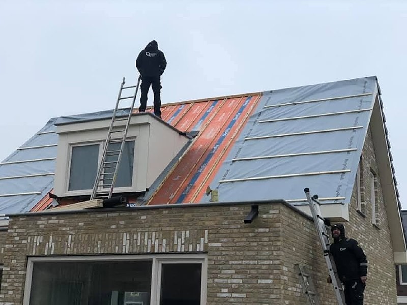 Twee vakmannen aan het werk op een schuin dak met dakkapel en dakfolie