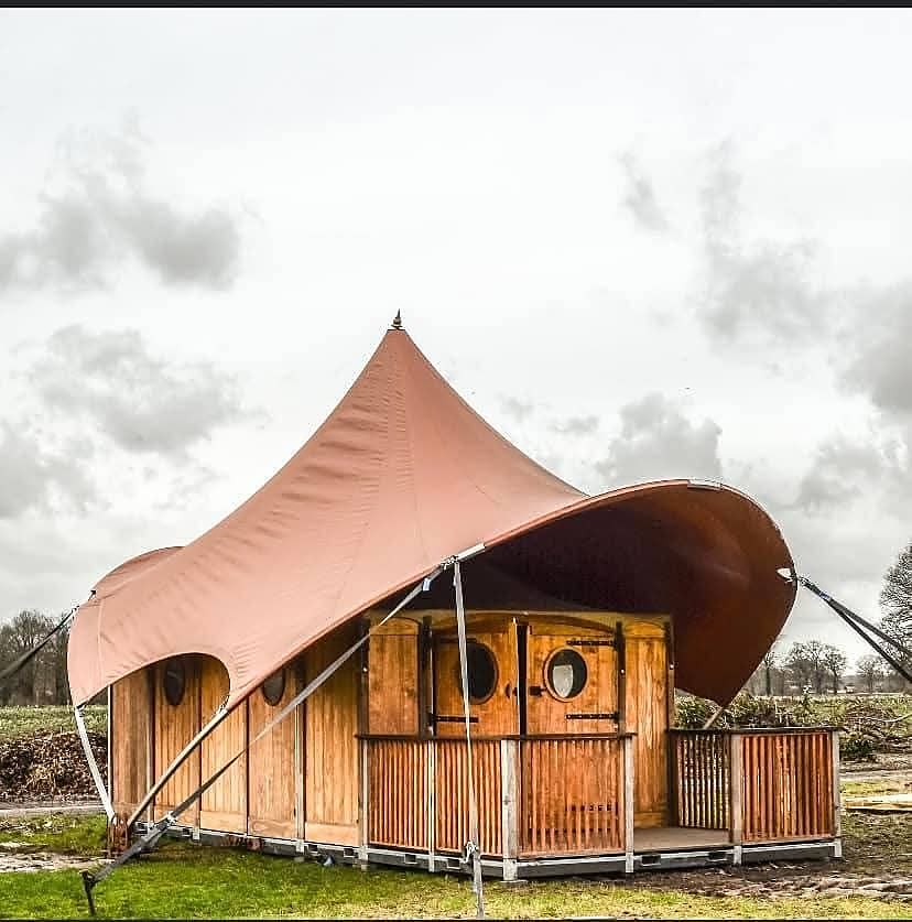 Houten glampingaccommodatie met ronde ramen onder een gespannen tentdoek