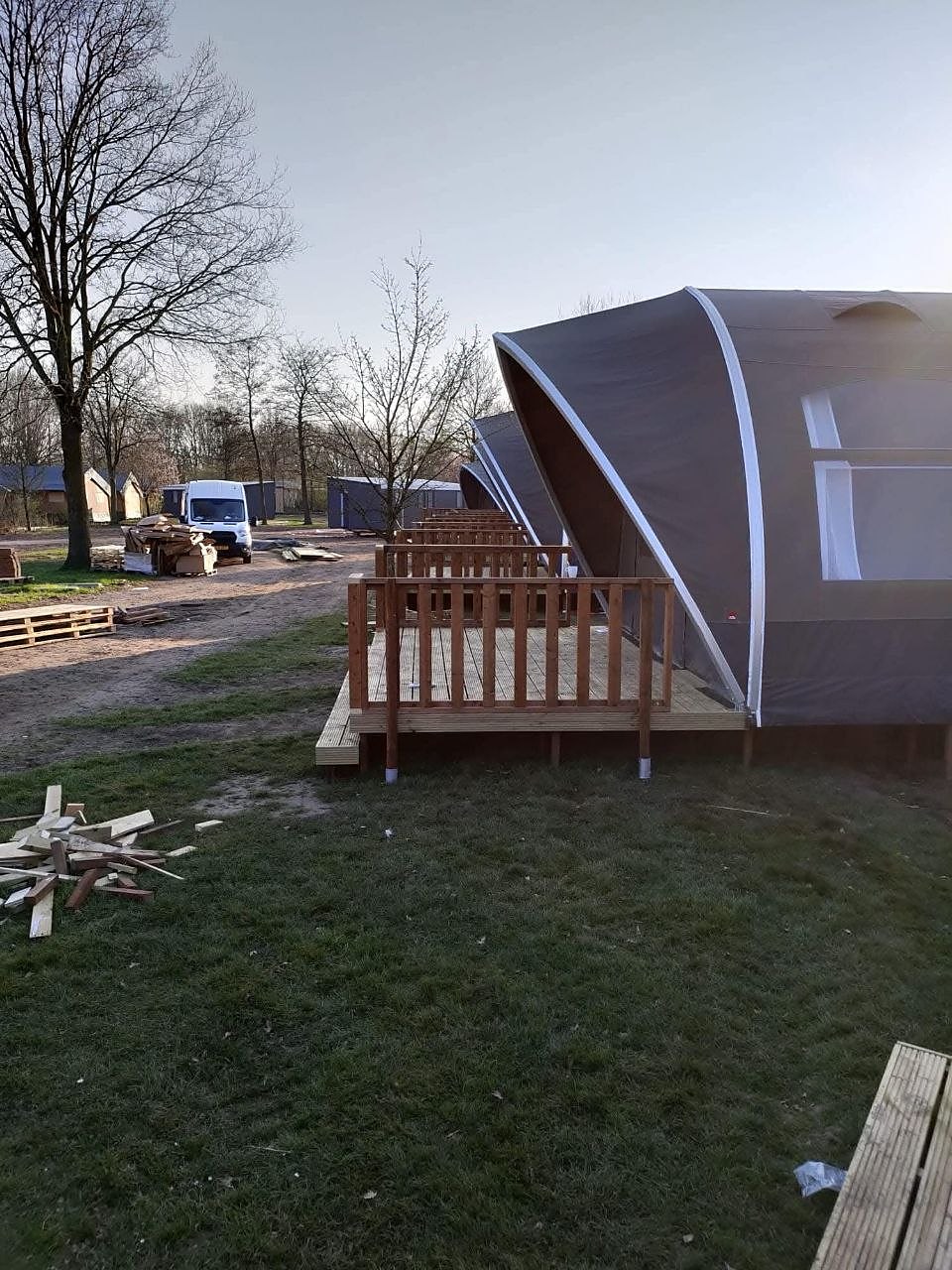 Rij glampingtenten met houten vlonders en hekwerk op een terrein in opbouw