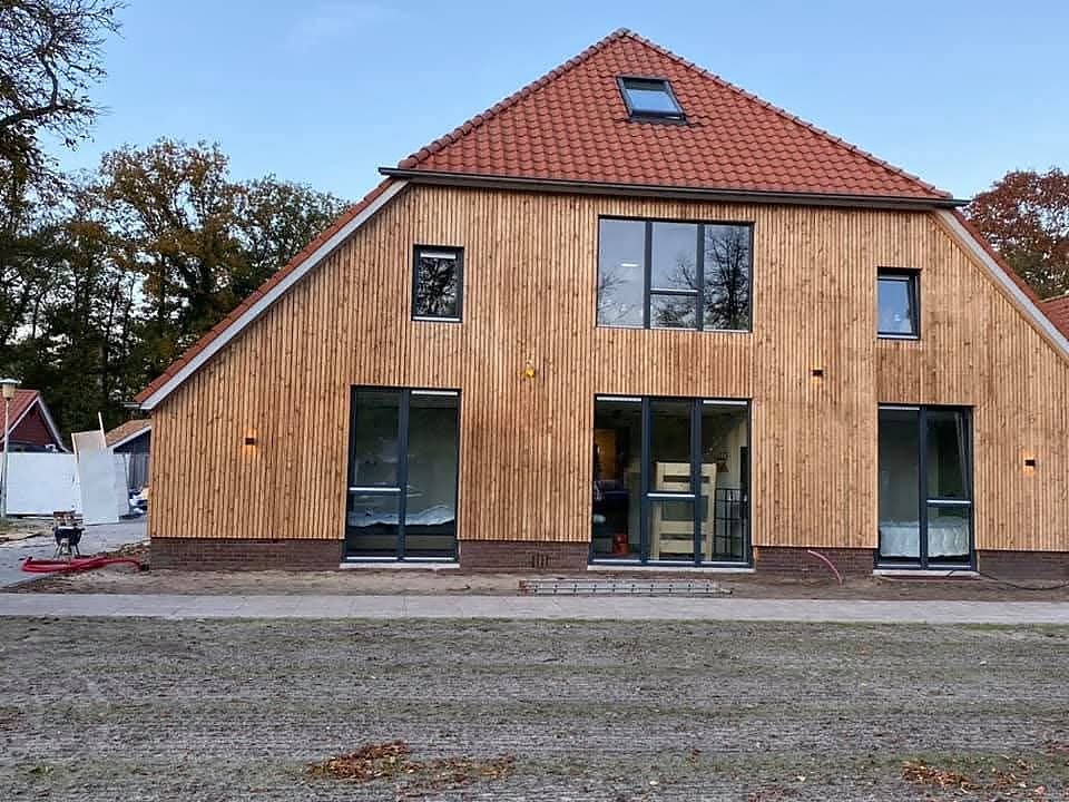 Woning met verticale houten gevelbekleding, grote glazen puien en een oranje pannendak