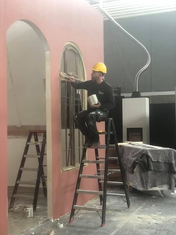 Vakman op een trap werkt aan een raamkozijn met boog in een interieur in afbouw