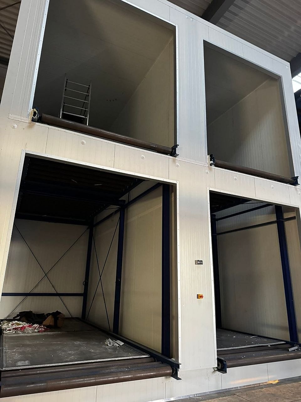 Gestapelde modulaire bouwunits met witte binnenwanden in een bouwhal