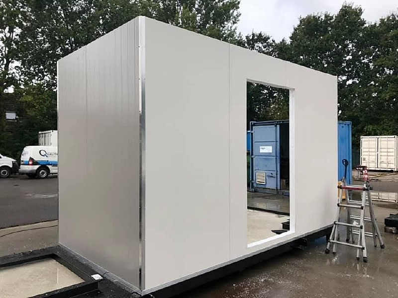 Modulaire unit van witte sandwichpanelen met raamopening, buiten op een bedrijfsterrein