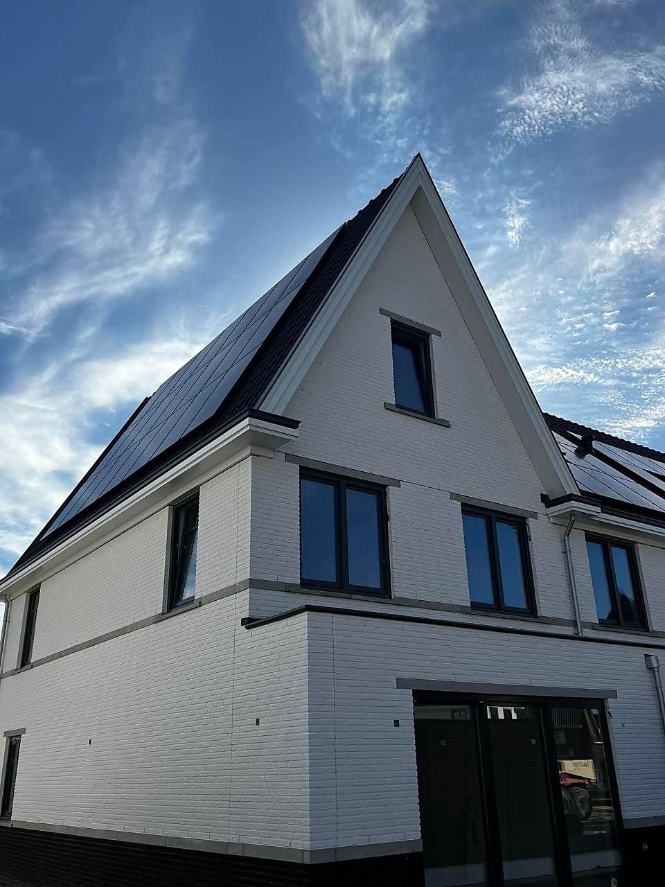 Witte woning met hoge puntgevel en zonnepanelen tegen een blauwe lucht