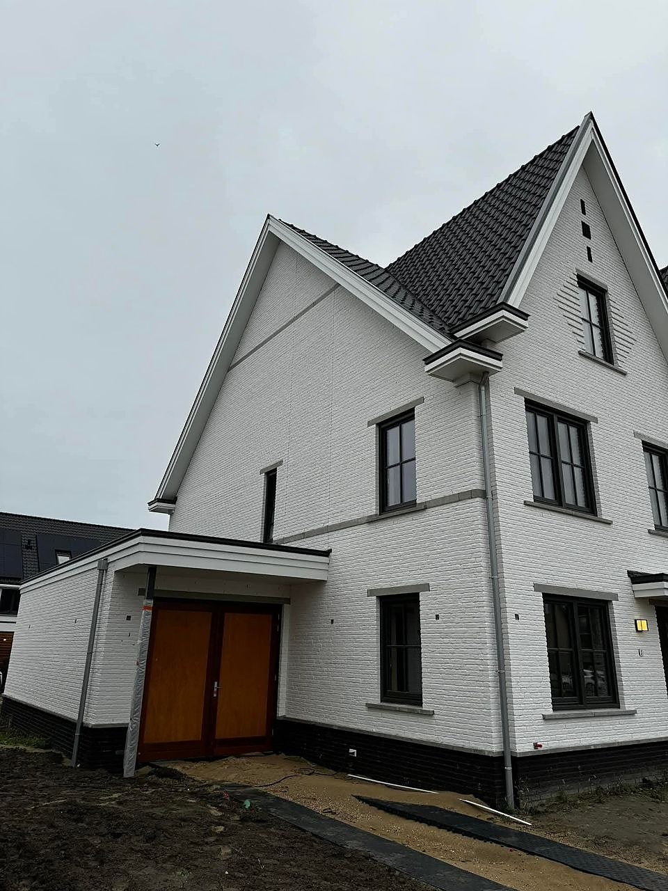 Witte woning met donker pannendak, zwarte kozijnen en houten garagedeuren