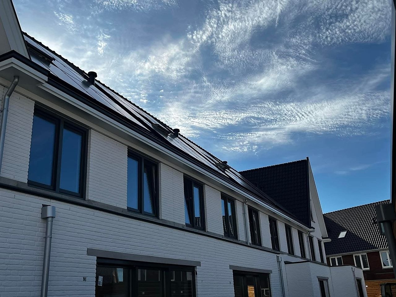 Rij witte woningen met zwarte kozijnen en zonnepanelen op het dak